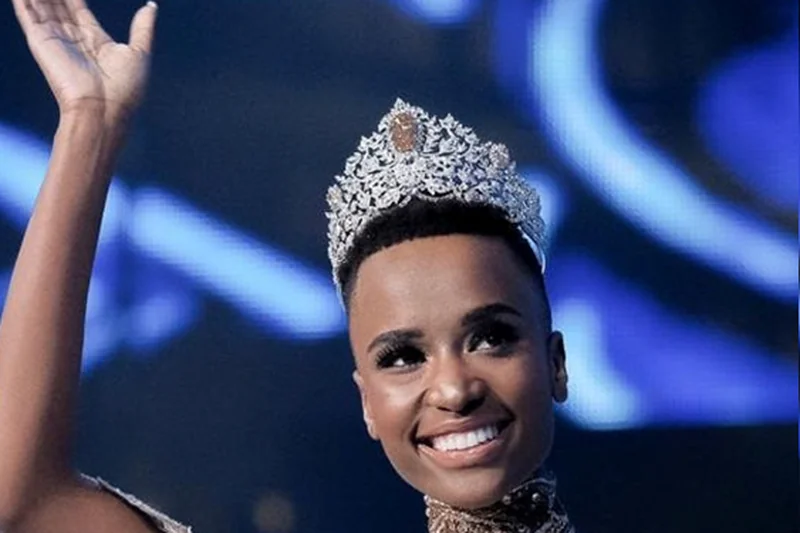 Zozibini Tunzi souriante avec couronne de Miss Univers et robe de scène argentée
