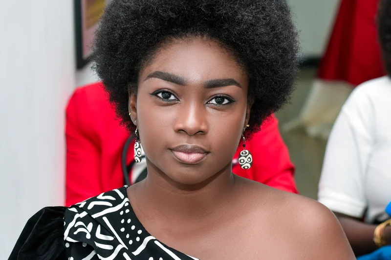 Hortavie Mpondo en portrait frontal avec afro court et robe noire a motifs blancs
