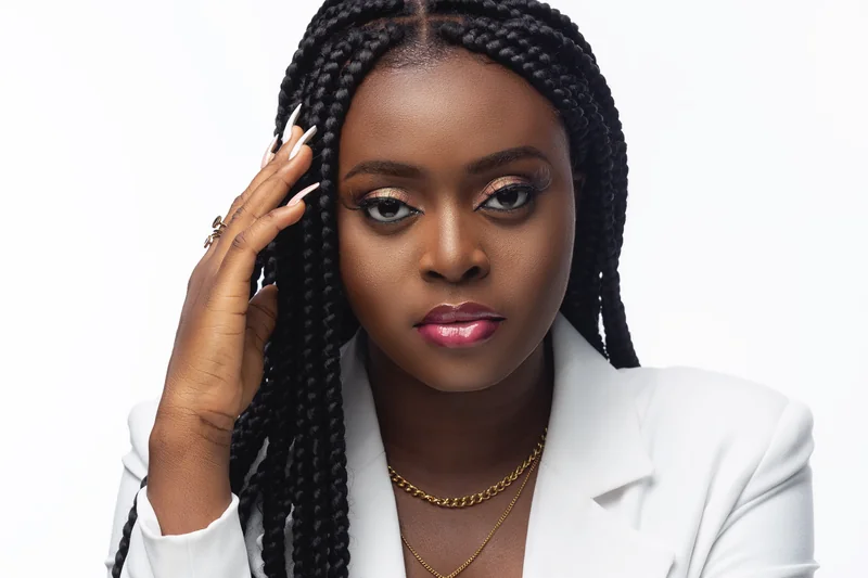 Morijah en portrait studio avec longues tresses, blazer blanc et maquillage rose