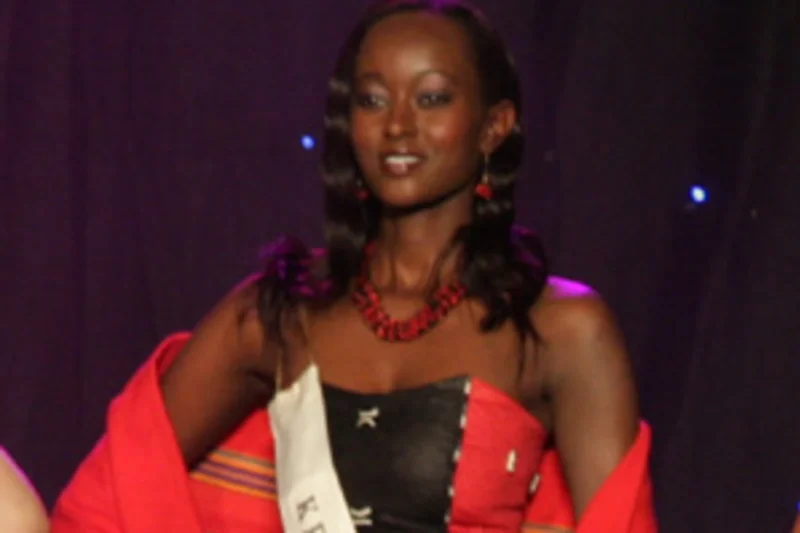 Ruth Kinuthia en tenue noire et rouge avec echarpe Kenya sur scene de concours