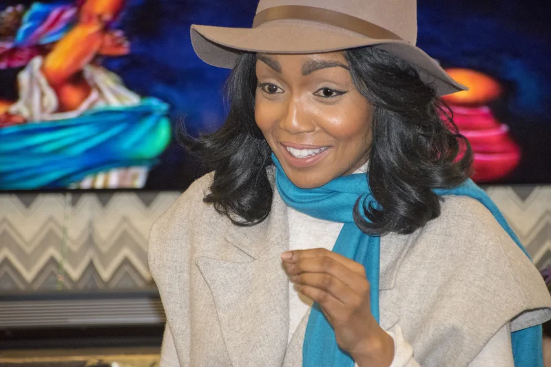Vicky Ngari-Wilson en chapeau beige et echarpe turquoise devant un fond colore