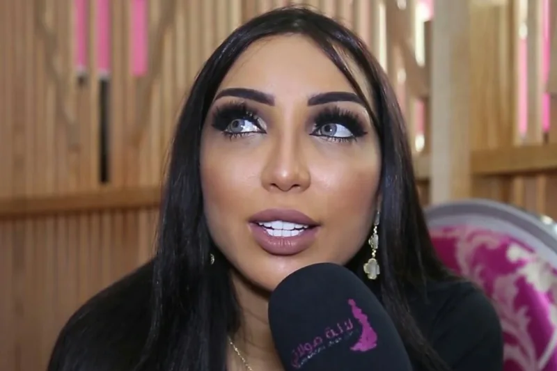 Dounia Batma avec cheveux noirs longs, maquillage intense et micro lors d'une interview