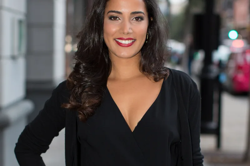 Nadia Kounda en combinaison noire, debout dans une rue avec sourire de tapis rouge