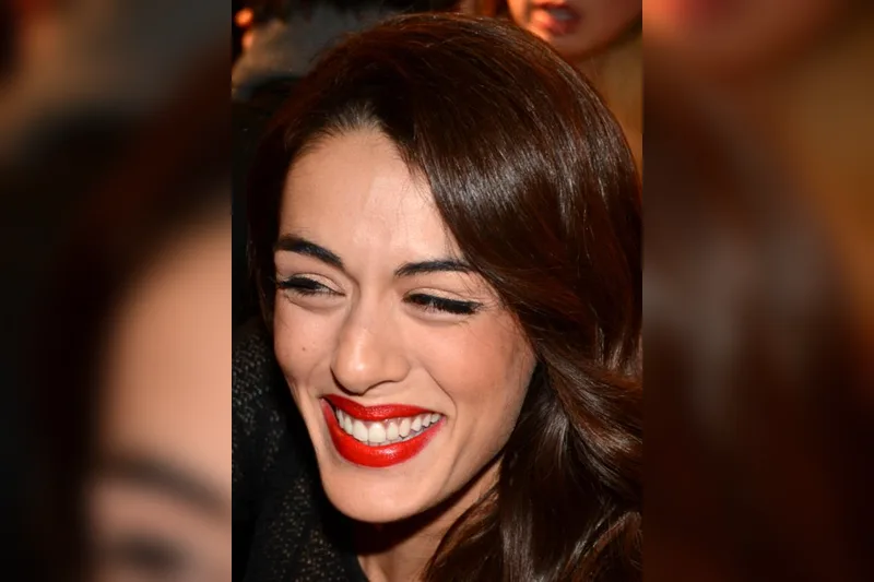 Sofia Essaïdi souriante avec rouge à lèvres rouge et cheveux bruns ondulés