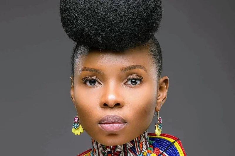 Yemi Alade en portrait studio avec coiffure afro haute, col perle colore et fond gris