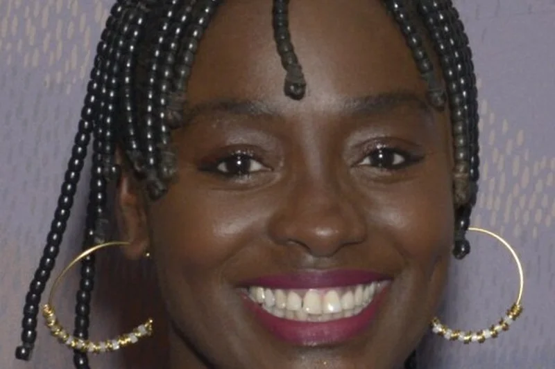 Aïssa Maïga souriante avec tresses fines, boucles d'oreilles dorées et haut bleu