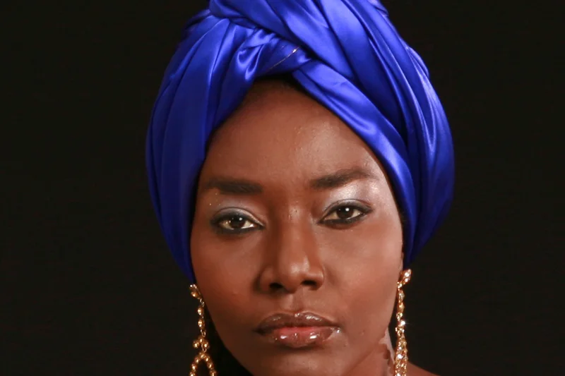 Coumba Gawlo Seck en turban bleu intense, bijoux dorés et regard frontal