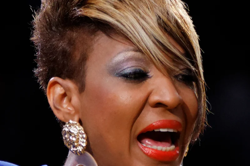 Viviane Chidid chantant avec coiffure courte blonde, boucles d'oreilles larges et robe bleue